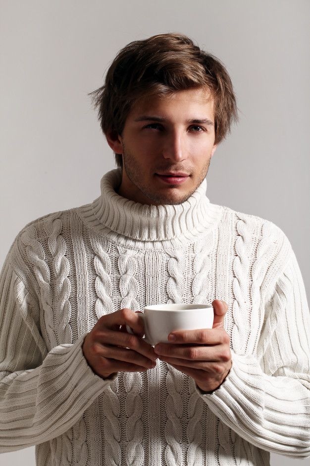 a man in a white sweater holding a coffee cup and looking at the camera while wearing a turtle neck sweater