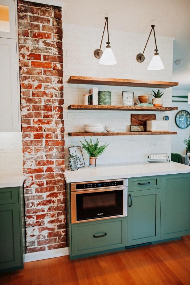 a kitchen with brick walls and green cabinets, white counter tops and open shelving above the stove