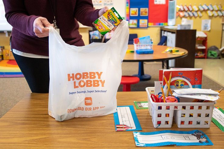 a woman is holding a bag full of school supplies in her hands while standing at a desk