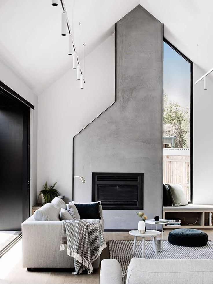 a living room with white furniture and a fireplace in the center, surrounded by large windows