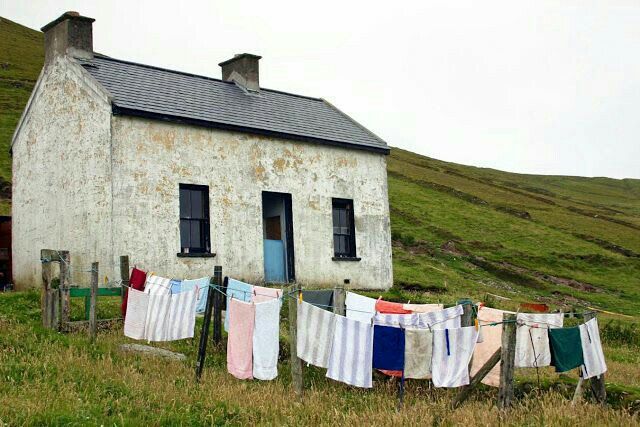 clothes hanging out to dry in front of an old house on the side of a hill