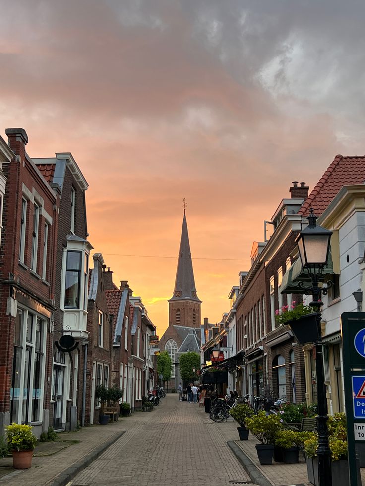 a city street lined with brick buildings and tall spires in the background at sunset