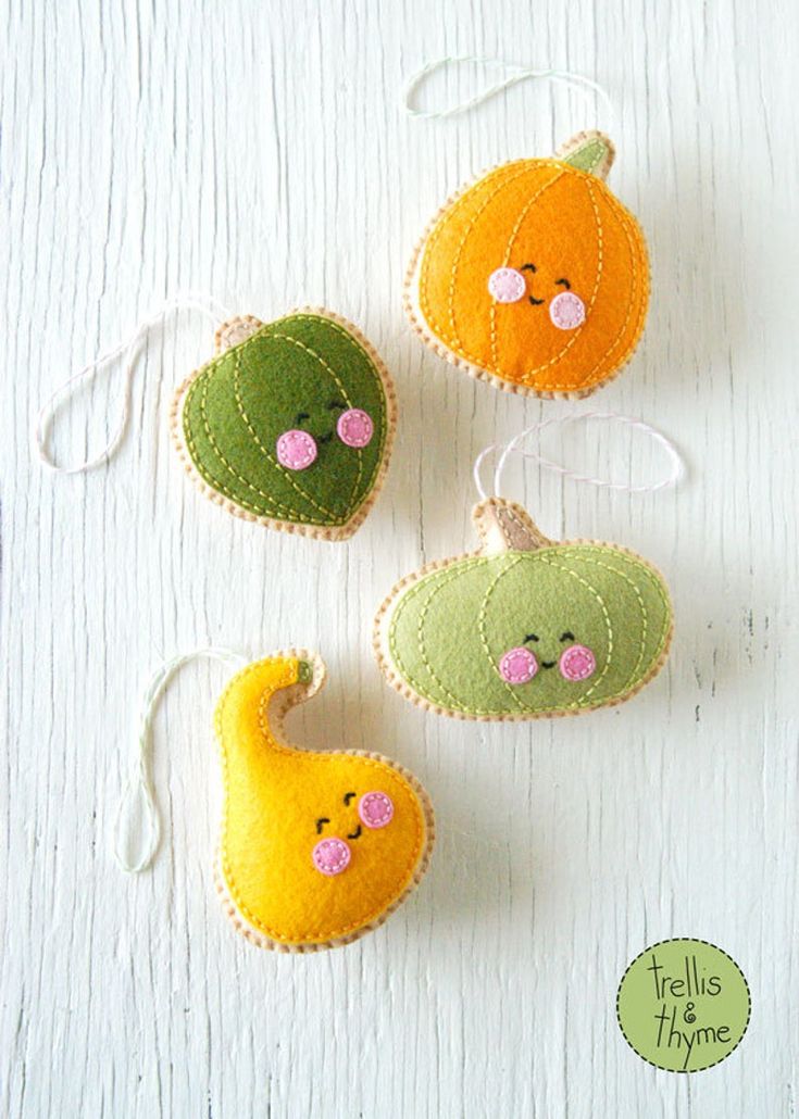 three felt pumpkins hanging from strings on a white surface