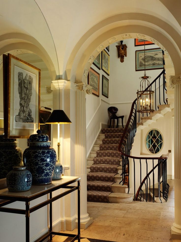 an entry way with stairs and pictures on the wall next to a table, vases and lamp