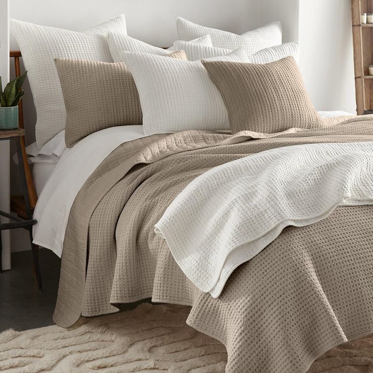 a bed with beige and white comforters in a small room next to a window