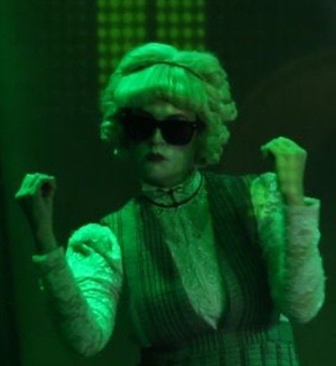 a woman with green hair wearing sunglasses and holding her hand up in front of her face