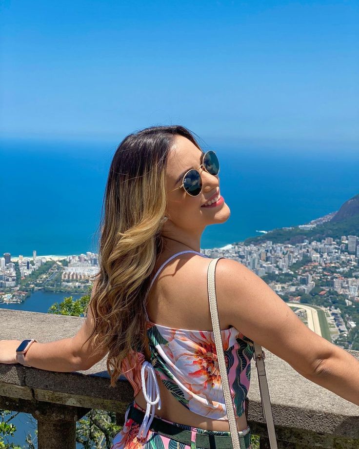 a woman standing on top of a wooden fence next to the ocean and buildings in the background