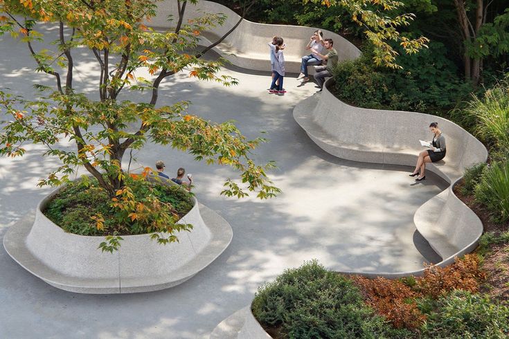 several people are sitting on concrete benches in a park with trees and bushes around them