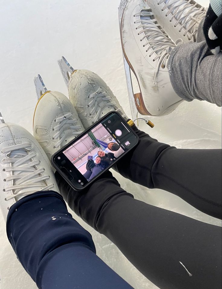 two people sitting in the snow with their feet up and one person holding an iphone