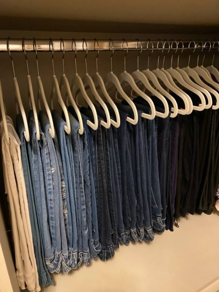 a closet filled with lots of jeans and pants hanging on clothes racks, all in different colors