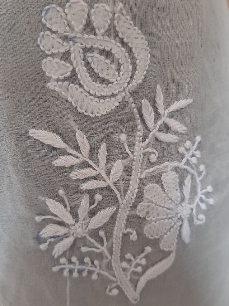 an embroidered flower on the back of a gray shirt with white threadwork and beads