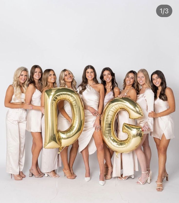 a group of beautiful women standing next to each other holding giant gold balloons in the shape of letters