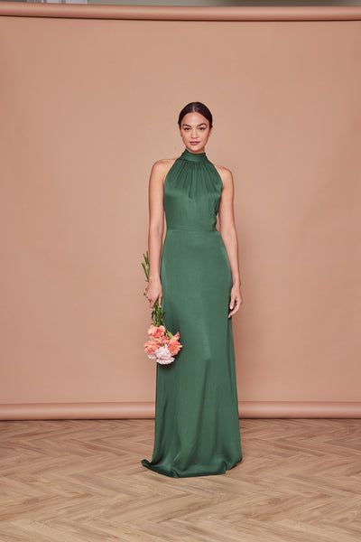 a woman in a long green dress standing on a wooden floor holding a flower bouquet