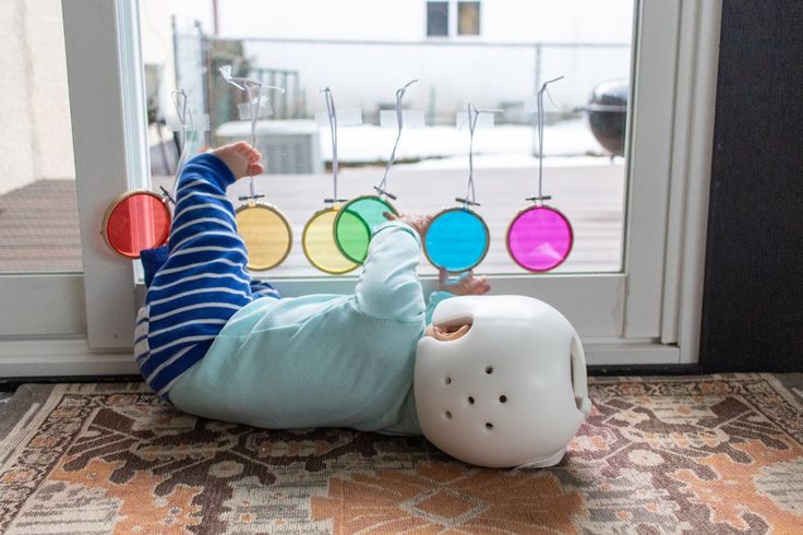 a toddler laying on the floor next to a window with colorful circles hanging from it