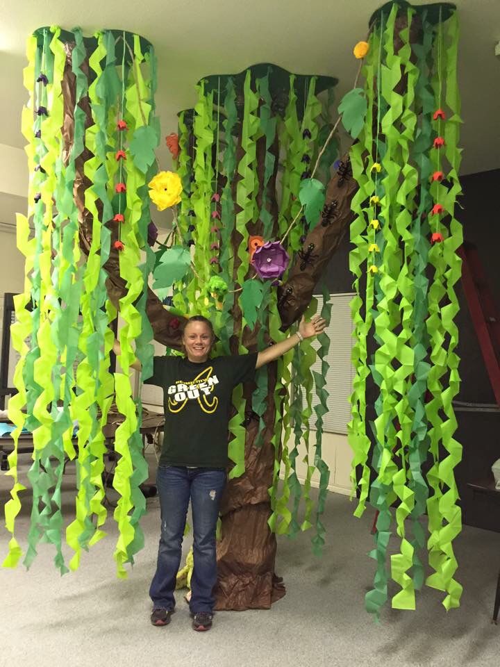 a person standing in front of a tree made out of green leaves and paper flowers