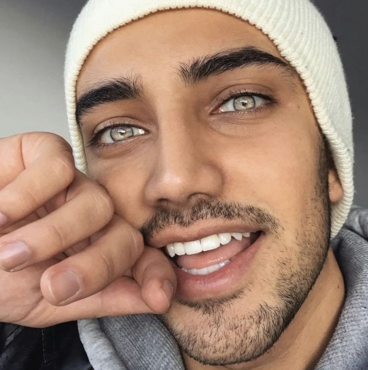 a man wearing a white beanie smiles at the camera while holding his hand up to his face