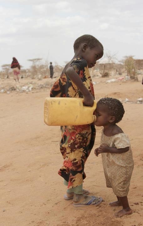 two young children standing in the dirt with a yellow container on their head and one holding a bottle