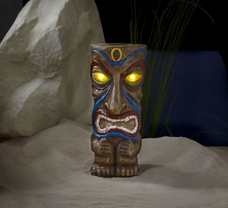 a tiki statue with glowing eyes and yellow eyes sits in front of a rock