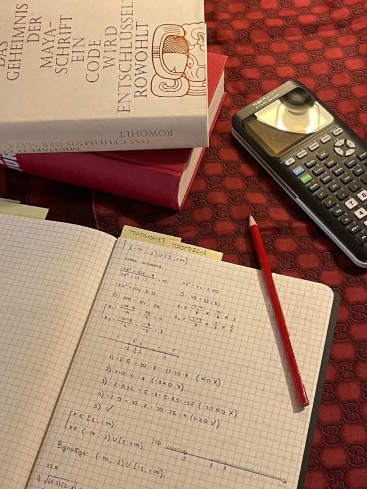 two notebooks and a calculator on a table with books, pen and phone