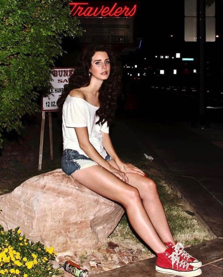 a young woman sitting on top of a rock next to flowers and a street sign