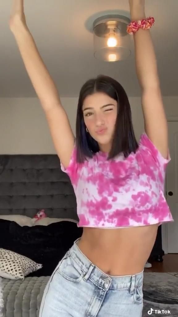 a young woman with her arms in the air while wearing jeans and a pink tie dye shirt