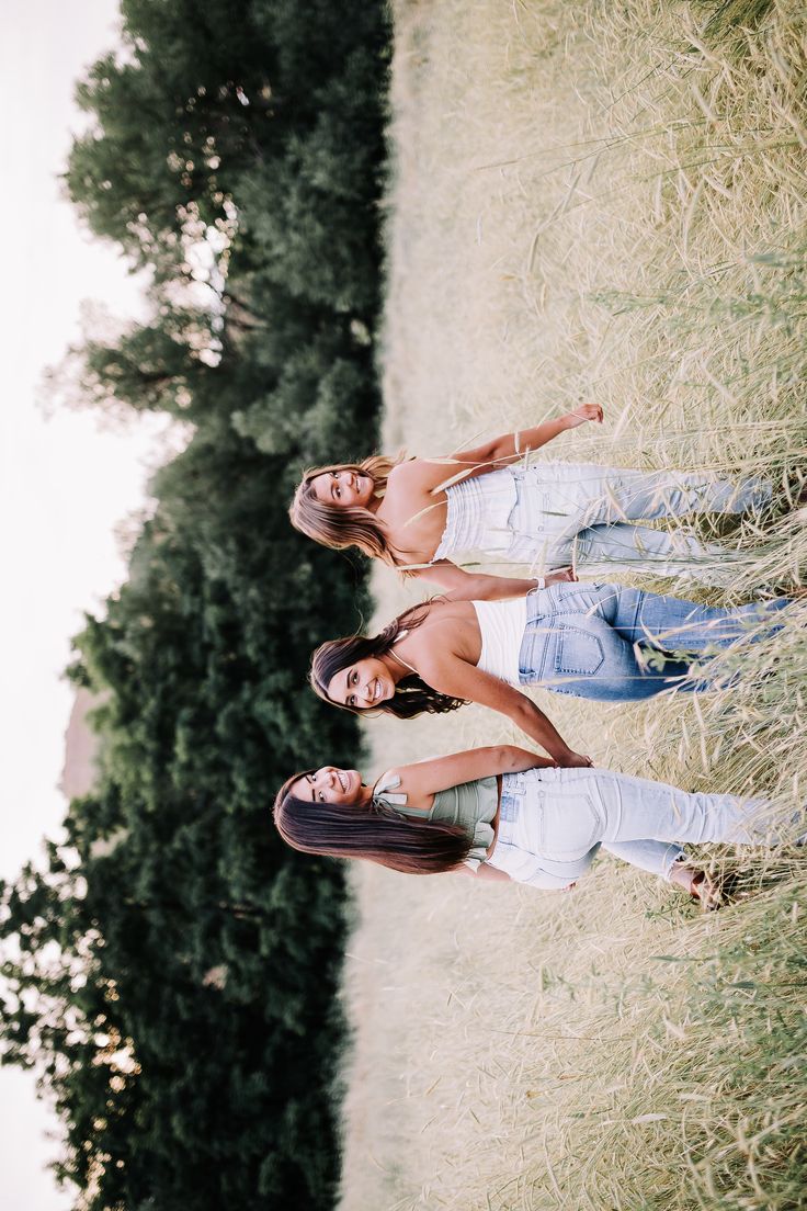 two young women standing next to each other in front of a tree and grass field