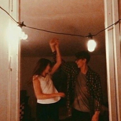 two people standing in a room with lights on the ceiling and one person raising his arm