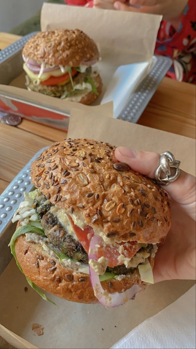 a person holding up a sandwich in front of two trays with sandwiches on them