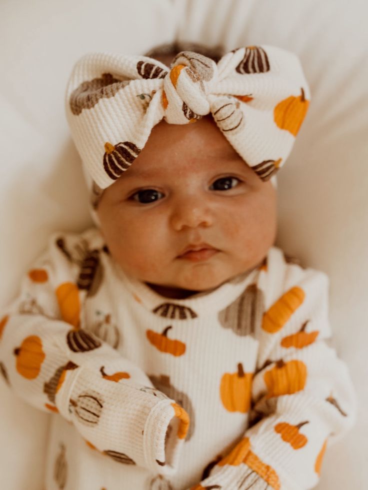 a baby wearing a white and orange outfit with a big bow on it's head