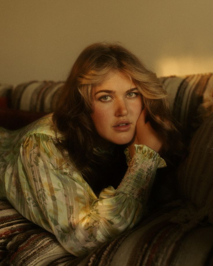 a woman laying on top of a couch next to a wall with her hands behind her head