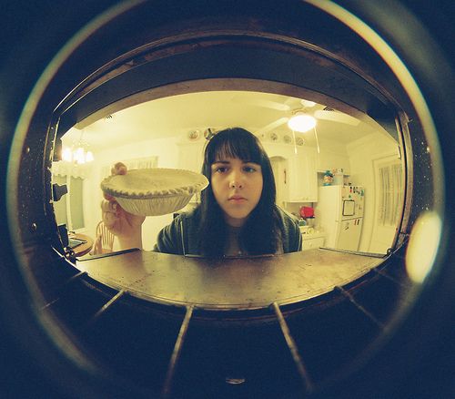 the reflection of a woman holding a bowl in front of her face is seen through a circular lens