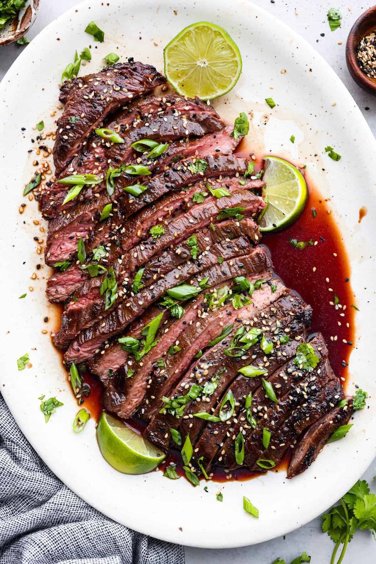 sliced steak with sauce and garnish on a white plate next to lime wedges