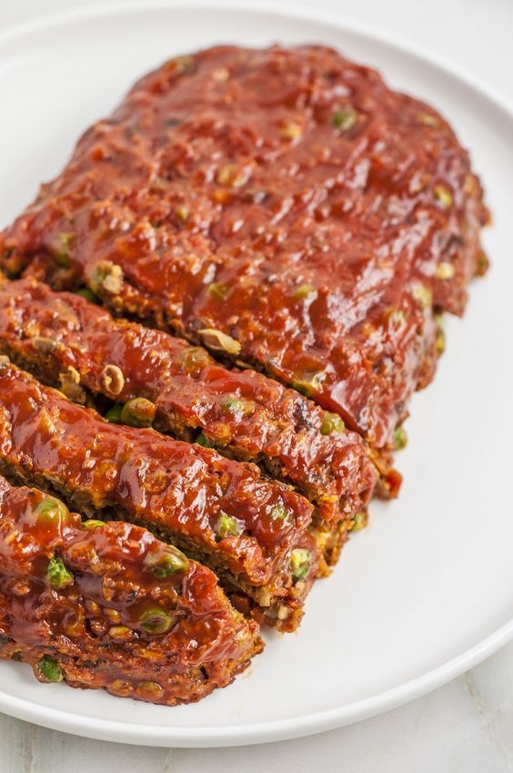 slices of meatloaf on a white plate with sauce and green pepper sprinkles