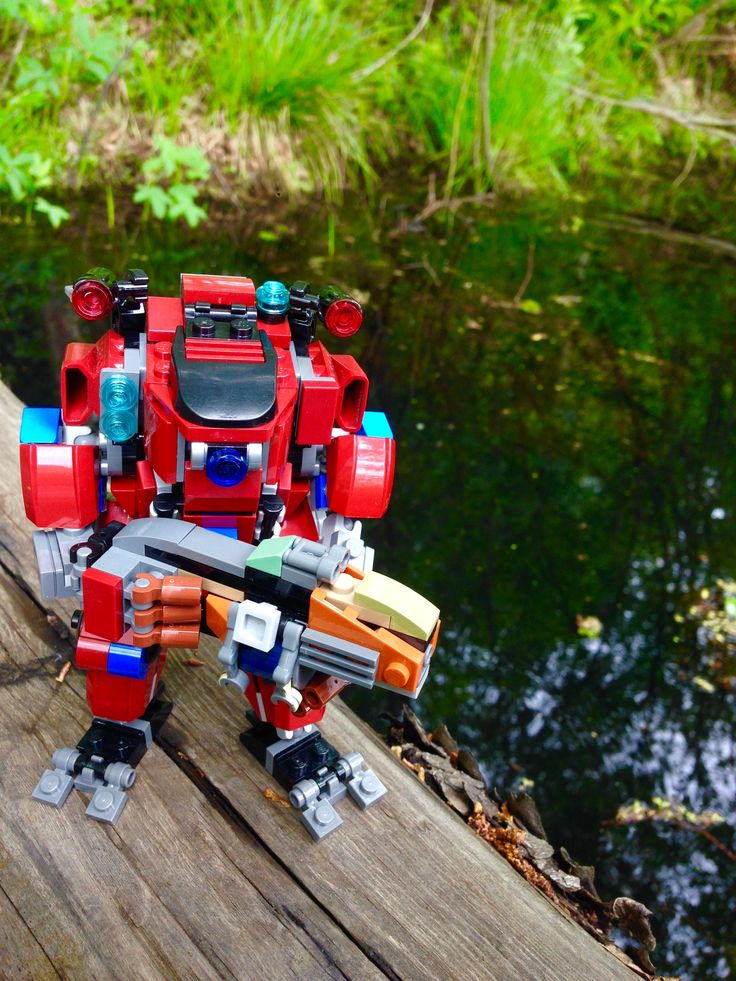 a toy that is sitting on top of a wooden plank next to water and trees