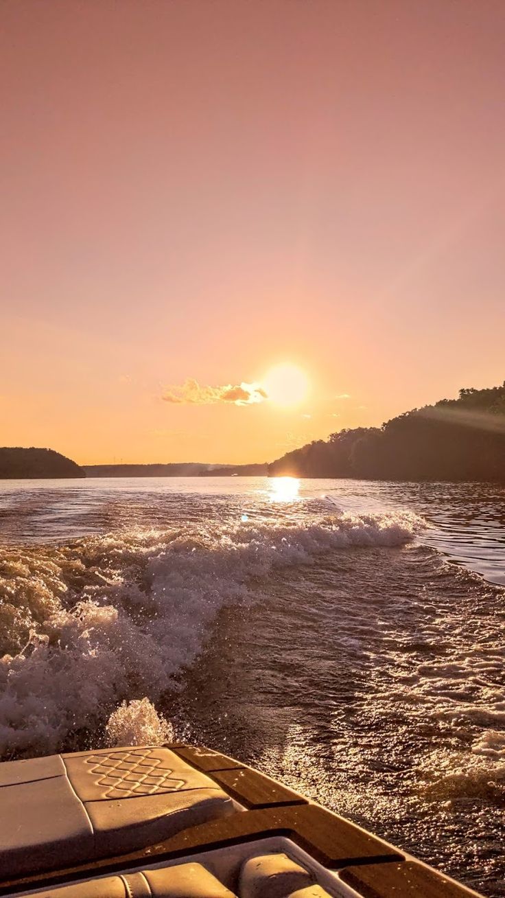 the sun is setting over the water from a boat in the ocean, with waves coming up to shore