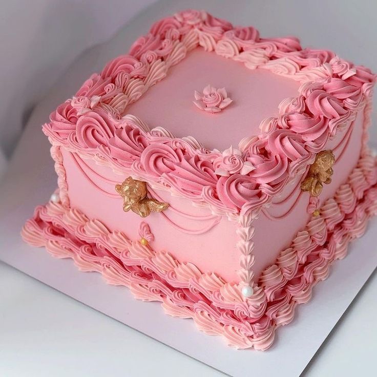 a pink square cake with flowers on the top and sides is sitting on a white surface