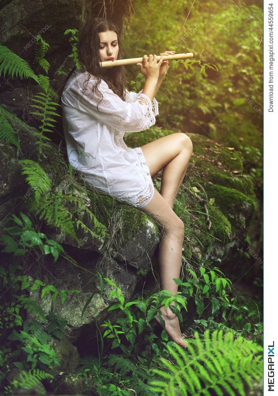 a woman sitting on top of a rock in the forest holding a flute to her mouth