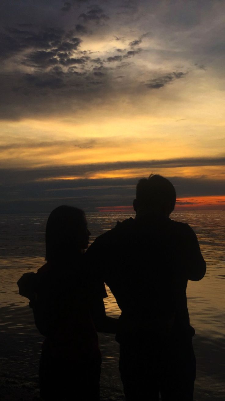 two people are standing on the beach watching the sunset