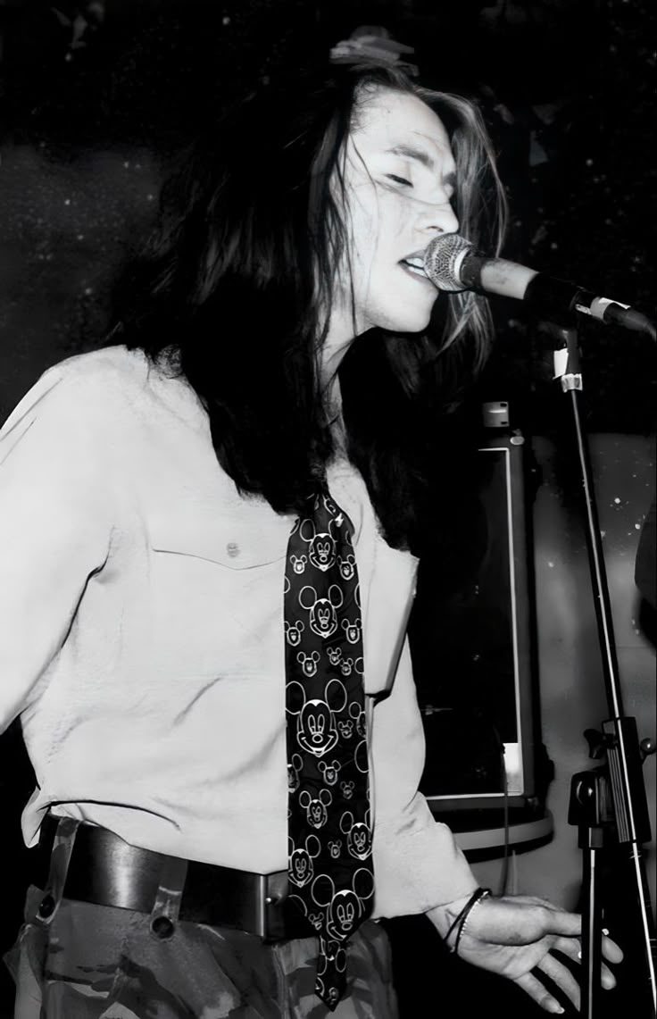 a woman singing into a microphone while standing next to a man with long hair wearing a tie