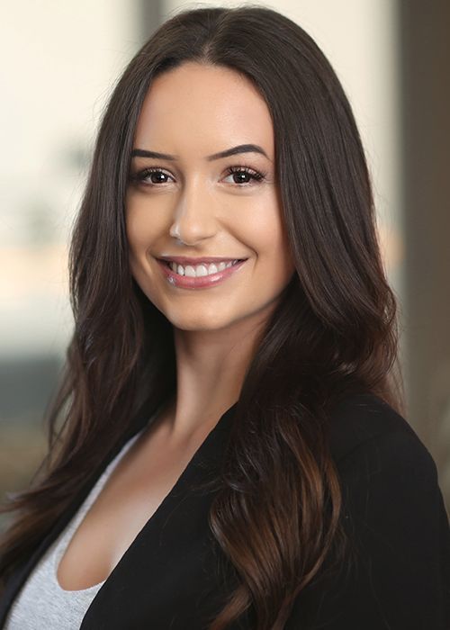 a woman with long brown hair smiling and wearing a black blazer over a gray shirt