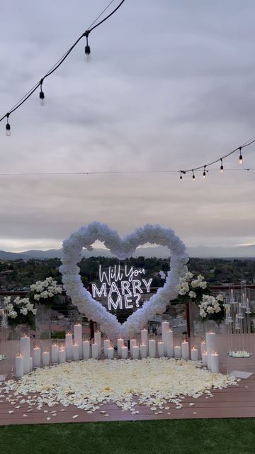 a heart - shaped sign that says will you marry me? surrounded by candles and flowers