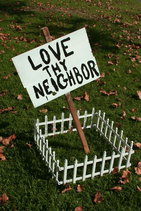 a sign that says love thy neighbor in front of some leaves on the ground and grass