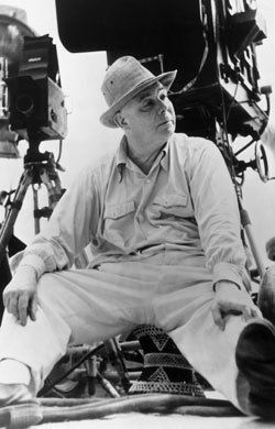 black and white photograph of an old man sitting in front of a camera on a boat