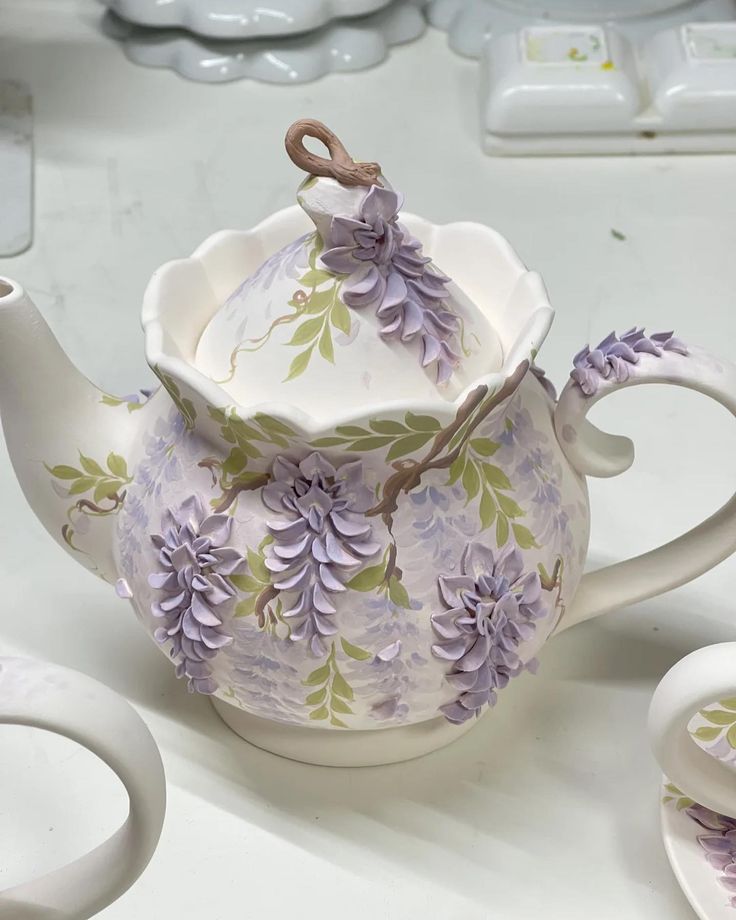 a tea pot with purple flowers on it next to two cups and saucers,