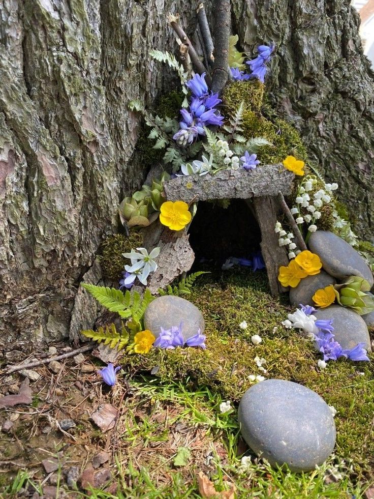 a tree stump with flowers and moss growing on the ground next to rocks in front of it