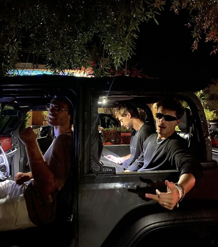 three men sitting in the back of a pick up truck at night with their hands out