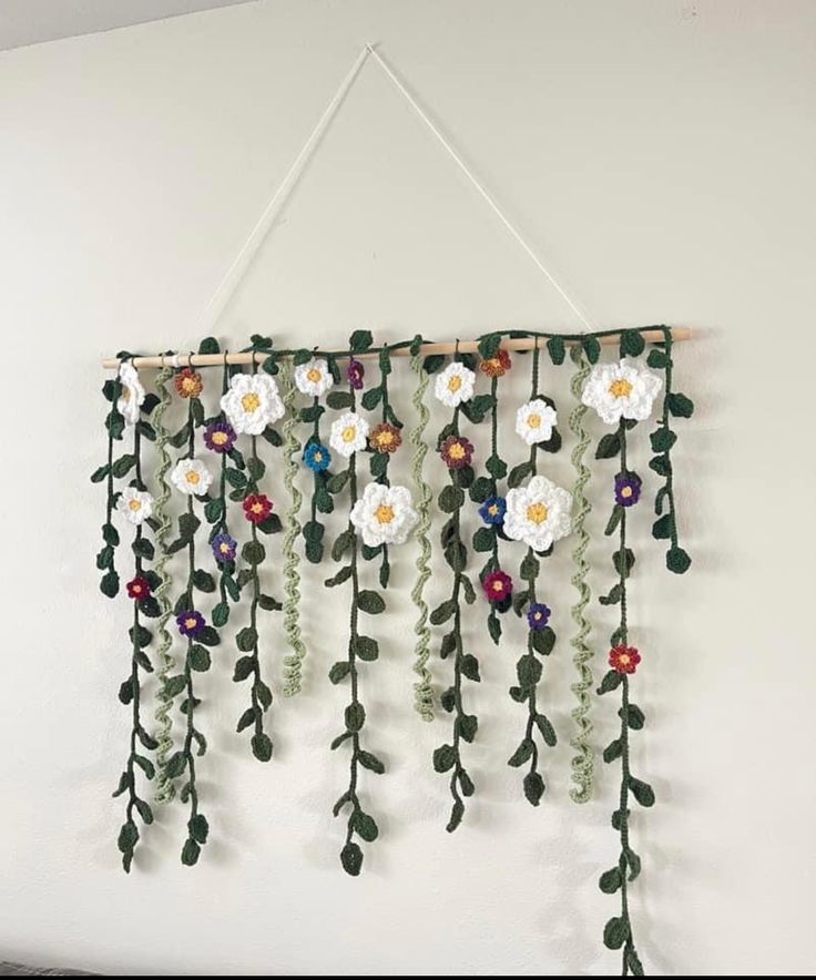 a white wall hanging with flowers and green leaves on it's side in front of a white wall