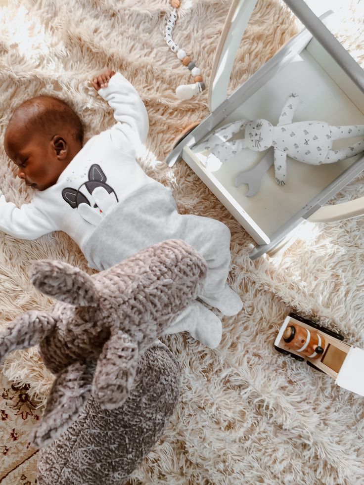 a baby doll laying on top of a white blanket next to a box and some toys