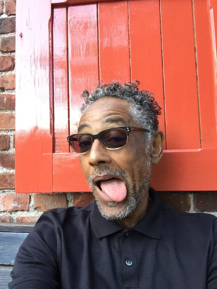 an older man sticking his tongue out in front of a red door with shutters