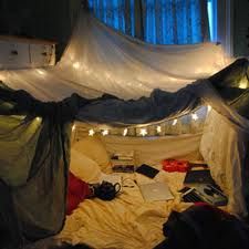 an unmade bed with white sheets and string lights on the ceiling, in front of a window